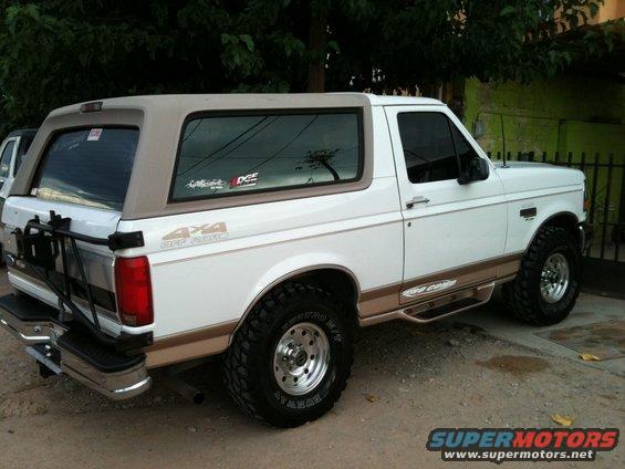 White Ford Bronco with tan top, 4x4 sticker on the side, and spare tire carrier on the back
