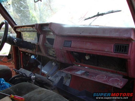 Red dashboard interior of an older vehicle, showing a steering wheel, instrument cluster, and vents