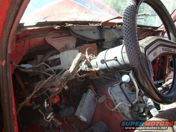 Damaged vehicle interior showing exposed wiring, steering column, and floor pedals