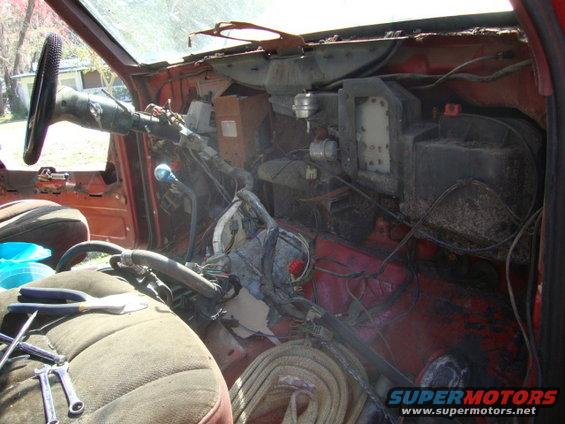 Interior of a vehicle with dashboard removed, showing exposed wiring and components. Tools are on the seat