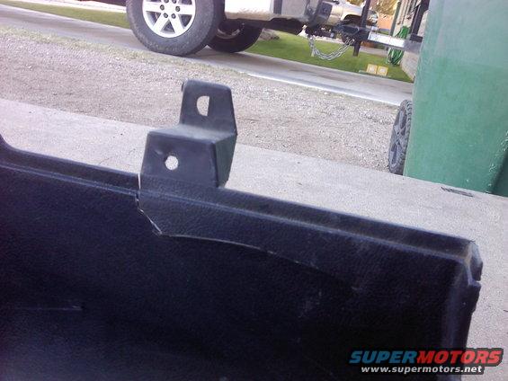 Black plastic car bumper section with a cracked metal mounting bracket. A white truck is visible in the background