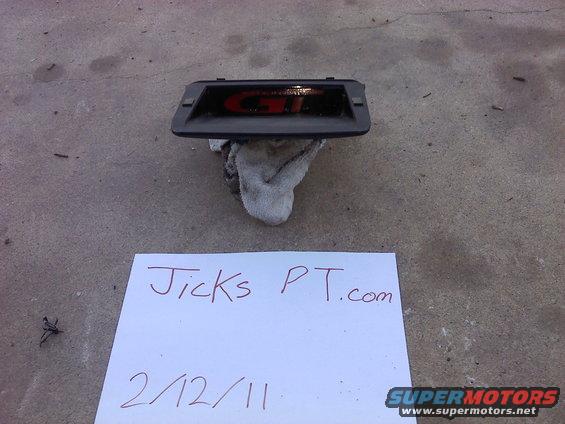 GT emblem on a black background, resting on a cloth. Paper with "Jicks PT.com" and "2/12/11" is in front