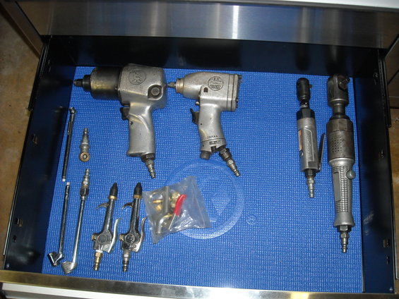 Collection of pneumatic tools including impact wrenches and a ratchet on a blue mat inside a metal drawer