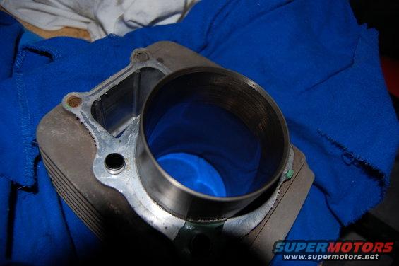 Engine cylinder with visible scoring on the interior wall, resting on a blue cloth