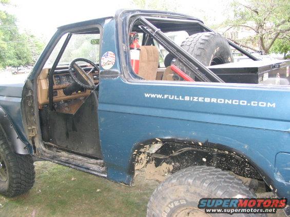Blue Ford Bronco with roll cage, spare tire, and "www.fullsizebronco.com" text on the side