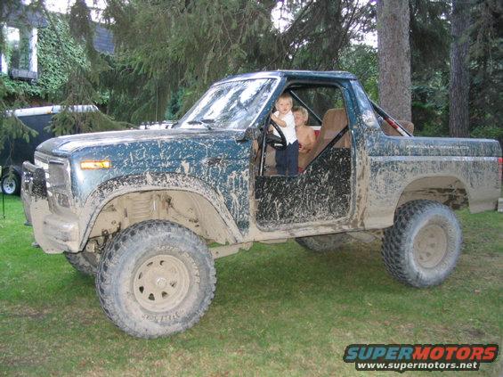 Mud-covered 1986 Ford Bronco with two children in the cab