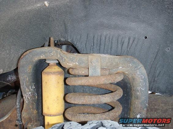 Rusty front suspension coil spring and yellow shock absorber, viewed from below