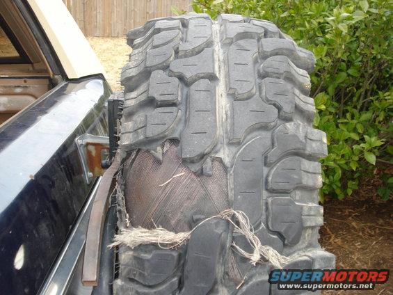 Damaged off-road tire on a dark vehicle, showing exposed internal structure and frayed cords