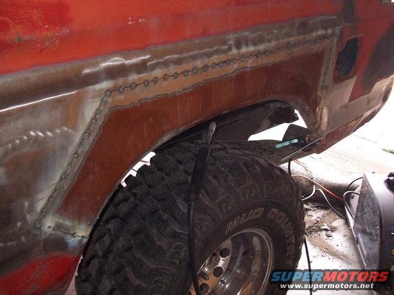 Close-up of red vehicle's rear fender area with fresh welds and a large off-road tire