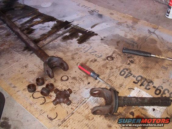 Driveshaft U-joint and yokes disassembled on a workbench with a screwdriver and other tools