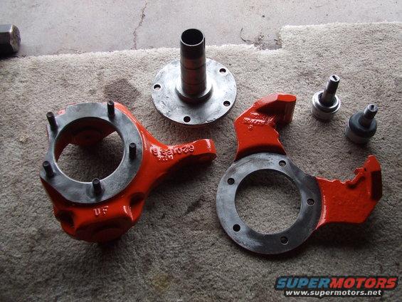 Two orange painted steering knuckles, a hub, and two ball joints laid out on a carpeted surface