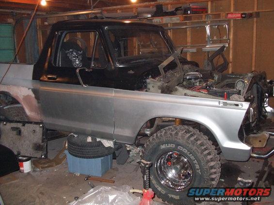 Silver and black Ford truck under repair, hood open, front fender removed, lifted suspension