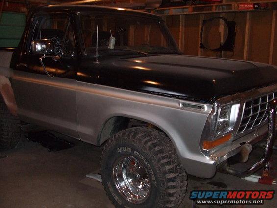 Ford Bronco with black top and silver body, lifted with off-road tires. Parked indoors