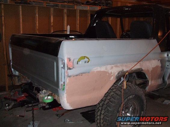 Rear quarter panel of a black and gray 1978 Ford Bronco undergoing bodywork, with primer and bondo visible