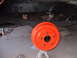 1979 Ford Bronco - A freshly painted orange brake drum is shown on jack stands with the vehicle's leaf springs visible above.