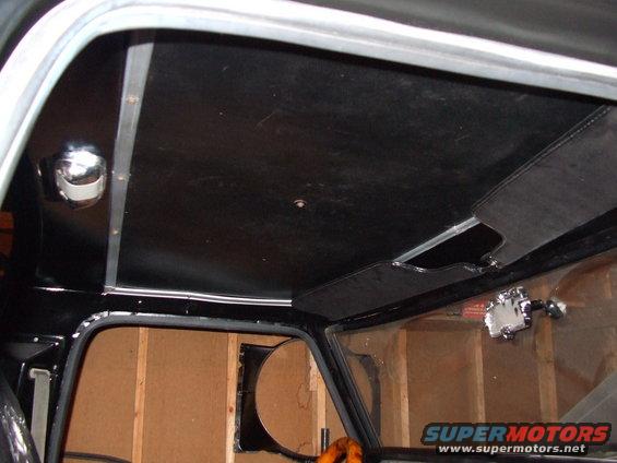 Interior view of a vehicle's headliner and window frame, showing wood-paneled walls in the background