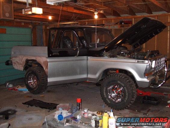 Ford F-Series truck in garage, hood up, undergoing repairs. Silver body, black top