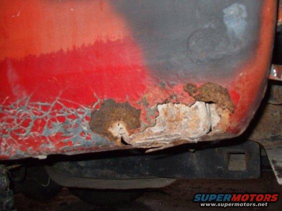 close-up of severe rust on a red vehicle's lower body panel
