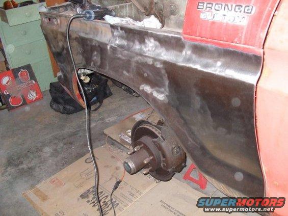 1979 Ford Bronco rear quarter panel undergoing bodywork, showing exposed metal and brake assembly