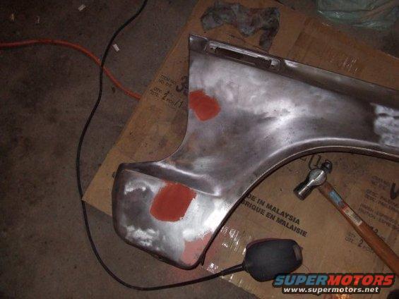 Bare metal fender section with red primer spots and a hammer