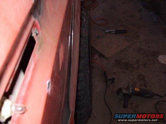 Red vehicle door with visible damage and a black tire next to it. An angle grinder and wires are on the floor