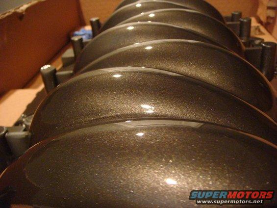 row of shiny, metallic brown engine intake manifold runners in a box