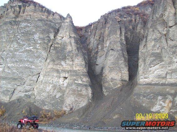 Red ATV parked by a river with a large rock formation in the background