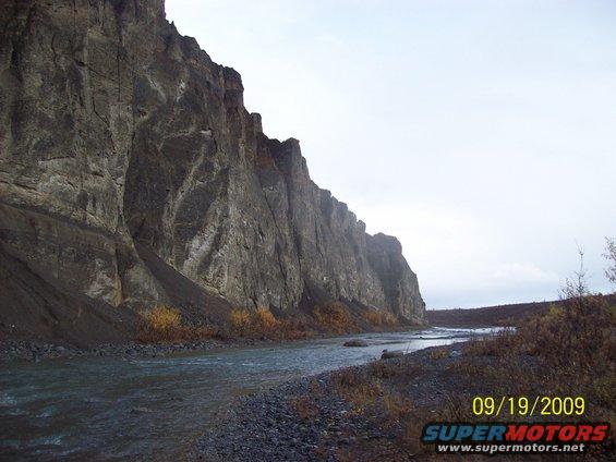 River flowing past a large cliff face with some sparse vegetation