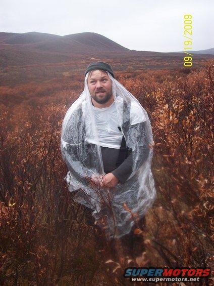 Man wearing a clear poncho over clothes stands in brush with hills in background. Date stamp reads 09/19/2009