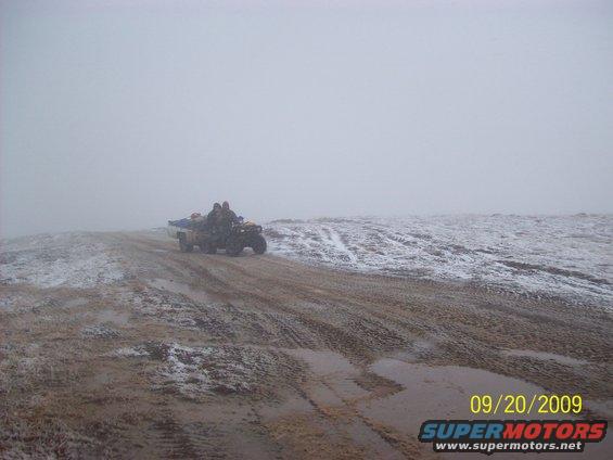 ATV with two riders on a muddy, snowy hill