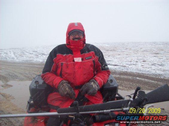 Guy in red snow gear on an ATV, with a rifle in front. It's snowing