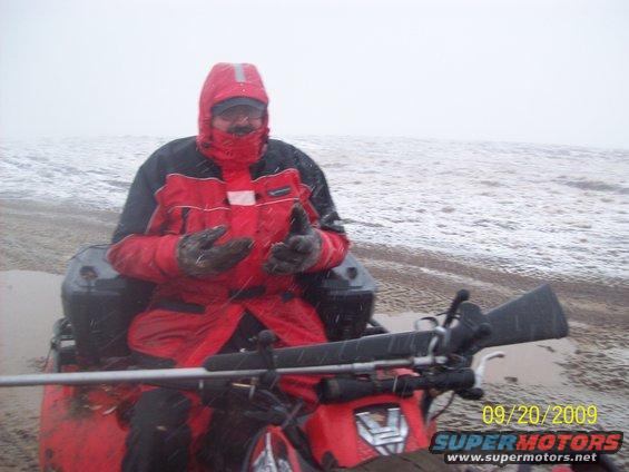Person in red jacket on red ATV with rifle mounted, snowy beach