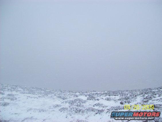 Snow-covered ground with sparse vegetation under a hazy sky. Watermark reads SUPERMOTORS