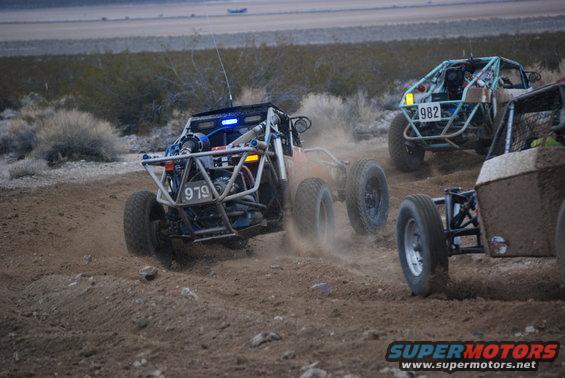 Off-road buggy with number 979 kicking up dust, seen from the front-left