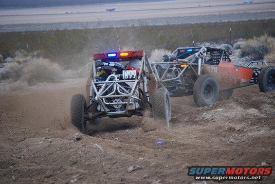 Two off-road buggies with light bars racing on a dirt track