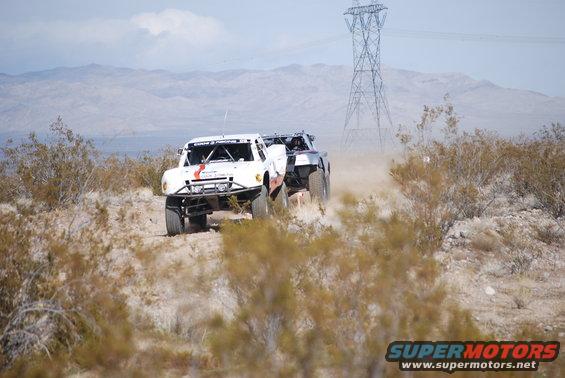 Two off-road trucks race through a dusty desert landscape