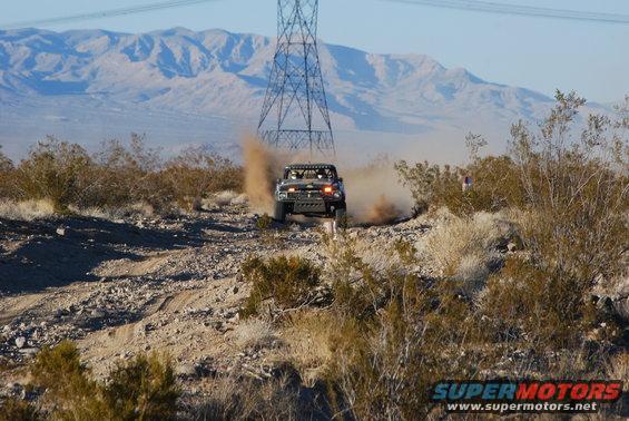 Off-road race truck kicking up dust on a desert track