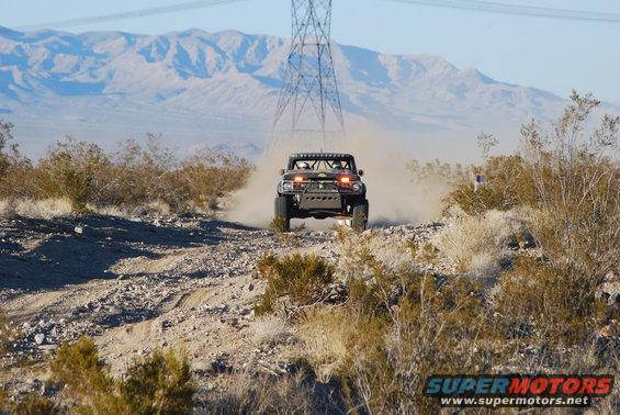 1982 Ford Bronco modified for off-road racing, kicking up dust on a desert trail