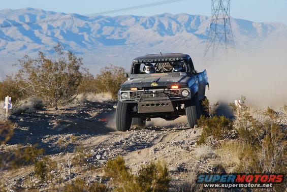 Modified pickup truck with roll cage and racing lights kicking up dust on a desert trail