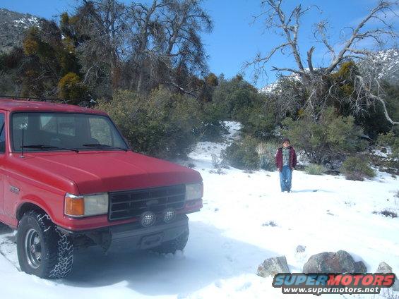 Red pickup truck parked in snow with a person standing in the background
