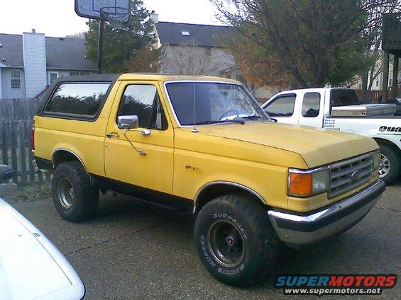 Yellow 1988 Ford Bronco parked in driveway next to a white pickup truck