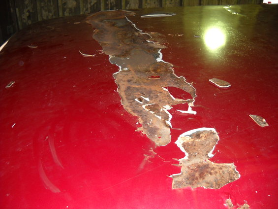 Red car roof with extensive rust damage and peeling paint