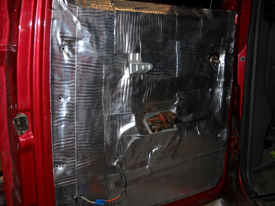 Car door panel removed, showing sound deadening material applied over the metal. Some wiring and a latch mechanism are visible