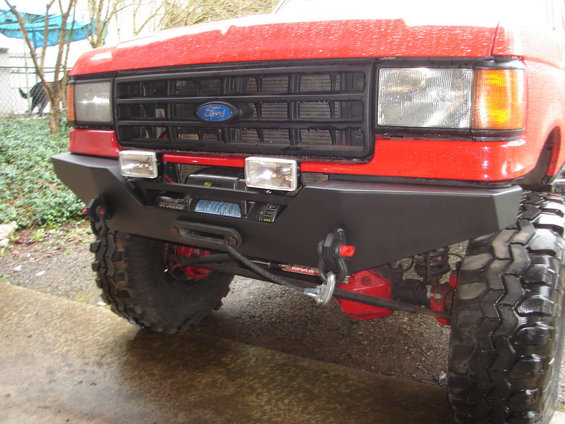 Red Ford truck front with aftermarket bumper, winch, and large tires