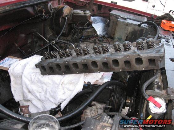 Engine cylinder head removed, showing valves and springs. Engine bay components visible