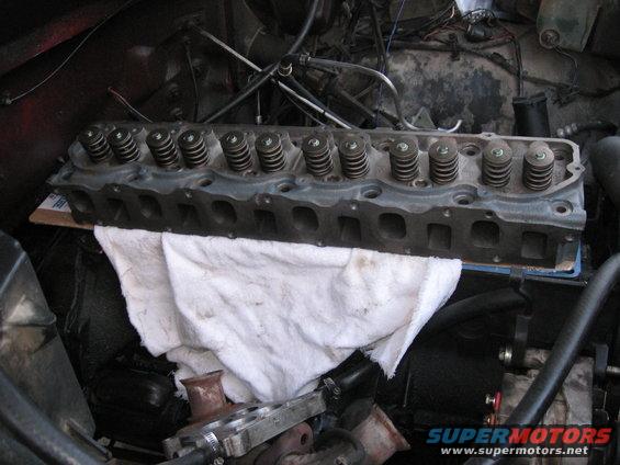 Engine cylinder head with valve springs visible, resting on a white cloth inside an engine bay