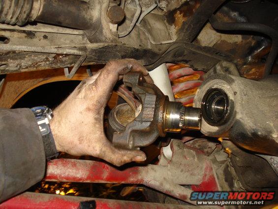 Mechanic's hands holding a U-joint assembly, with drivetrain components visible