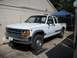 1994 Ford Explorer - A white pickup truck with a dual cab is parked on ramps in front of a building.
