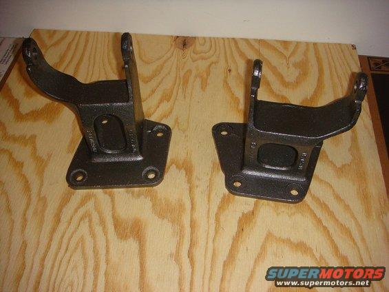 Two black cast iron engine mounts on a plywood surface. Text is visible on the mounts