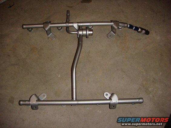 Fuel rail assembly with injectors attached, resting on a concrete floor